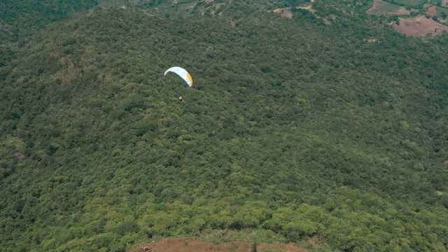 Amazing aerial video of flying paraglider on the background of wild nature. Paraplan drifting above the green tropical trees. Extreme sport. Hipster modern hobby concept. Paraplane flying in the sky.