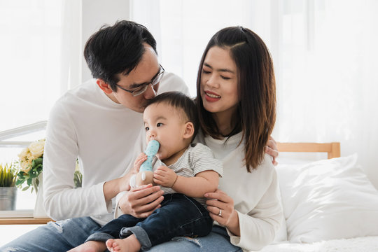 Happy asian family parents hug and kissing their baby boy in bedroom