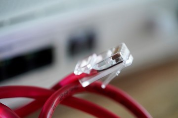 close up of red netwrok cable with connector by blurred internet router