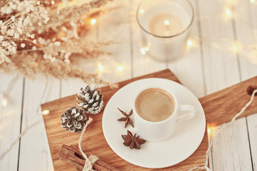 Cup of coffee with a garland lights, burning candle and decoration on table. Cozy home concept