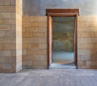 Open wooden door in bricks stone wall revealing vacant room with bricks wall