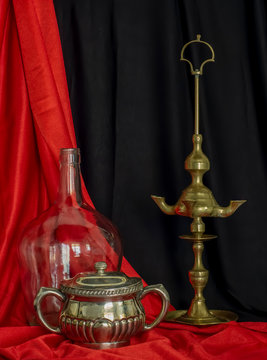 Old Spanish Oil Lamp Glass Demijohn and Silver sugar Bowl Red and Black Background Still Life