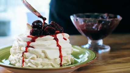 Chef cooking meringue cake, close-up. Cook puts a cherry jam on top of meringue while preparing sweet dessert.