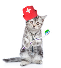Kitten dressed like a doctor with stethoscope on his neck and medical hat holds toothbrush. isolated on white background
