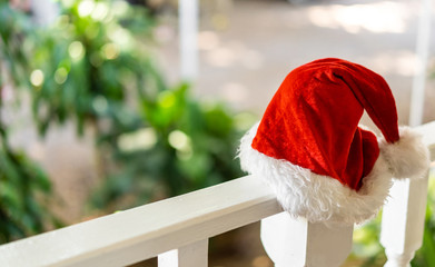 new year red santa claus hat in summer on a white fence against a tropical green
