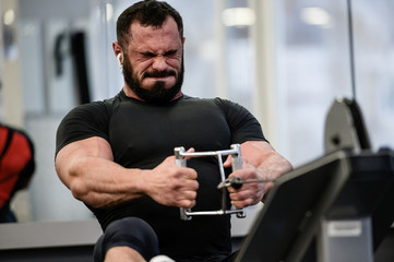 hard stress motivation sport workout training of bearded strong man with big muscles pulling weight on exercise equipment with grimace of pain and effort on face in gym