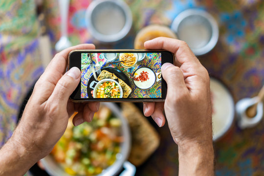 A man takes a photo of food on his smartphone in the summer at a breakfast cafe. Share your lifestyle on a social network.