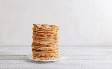 Cooking pancakes. Shrovetide (Maslenitsa) - blini stack on a blue plate on a wooden table.