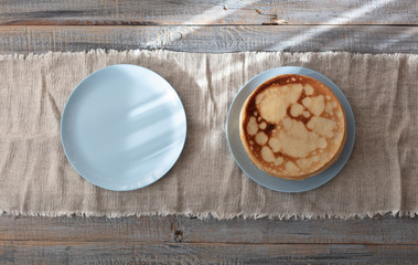 Cooking pancakes. Shrovetide (Maslenitsa) - blini stack on a blue plate on a wooden table.