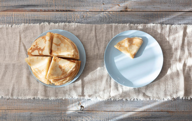 Cooking pancakes. Shrovetide (Maslenitsa) - blini stack on a blue plate on a wooden table.