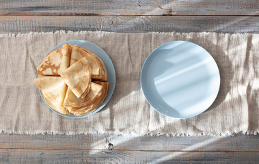 Cooking pancakes. Shrovetide (Maslenitsa) - blini stack on a blue plate on a wooden table.