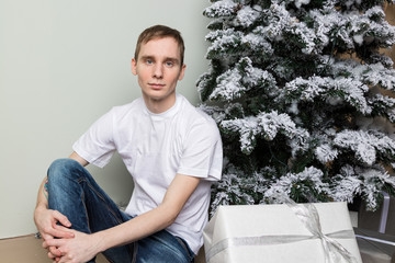 Young man with big present sitting on floor near christmas tree