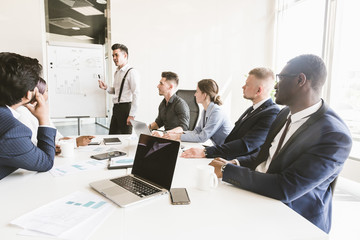 Company leader standing near the flipchart. A team of young businessmen working and communicating together in an office. Corporate businessteam and manager in a meeting