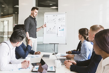 Company leader standing near the flipchart. A team of young businessmen working and communicating together in an office. Corporate businessteam and manager in a meeting
