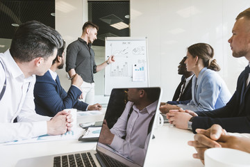 Company leader standing near the flipchart. A team of young businessmen working and communicating together in an office. Corporate businessteam and manager in a meeting