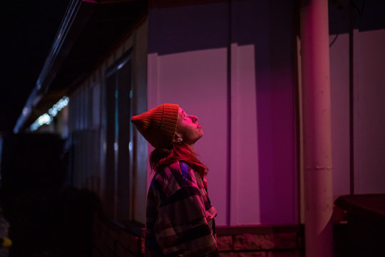 A young woman in a winter hat under a pink light from a cheap motel sign