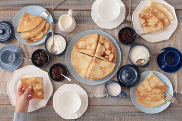 Shrovetide (Maslenitsa) - breakfast with blini stack, jam and sour cream with tea or coffe on bare plates on a wooden table.