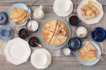 Shrovetide (Maslenitsa) - breakfast with blini stack, jam and sour cream with tea or coffe on bare plates on a wooden table.