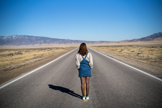 A young woman in vintage clothes stands in the middle of the road in nowhere