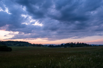 The colors of the sky after sunset with clouds above the mountain meadow.