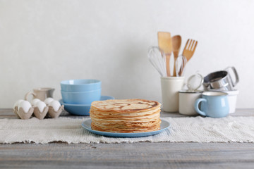 Cooking pancakes. Shrovetide (Maslenitsa) - blini stack on a blue plate on a wooden table.