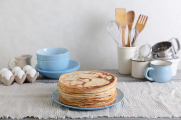 Cooking pancakes. Shrovetide (Maslenitsa) - blini stack on a blue plate on a wooden table.