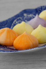 Meringues, various colours, on a patterned blue and white plate.  Grey wood background