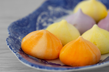 Meringues, various colours, on a patterned blue and white plate.  Grey wood background