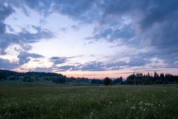 The colors of the sky after sunset with clouds above the mountain meadow.