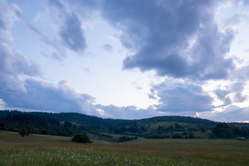 The colors of the sky after sunset with clouds above the mountain meadow.