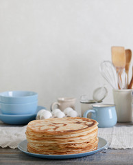 Cooking pancakes. Shrovetide (Maslenitsa) - blini stack on a blue plate on a wooden table.
