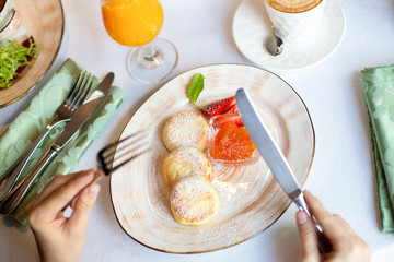 Cheesecakes, baked polpettine di ricotta on a plate with jam and strawberries. On the table is a cup of coffee, a glass of orange juice, a fork and a knife in hand