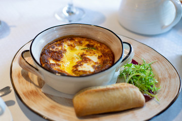 Breakfast Italian omelet baked with cheese on a plate with bread and green salad on a table with a glass of orange juice.