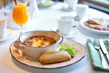 Breakfast Italian omelet baked with cheese on a plate with bread and green salad on a table with a glass of orange juice.