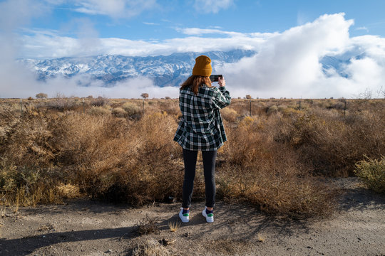A woman in a vintage flannel shirt takes a photo with her phone of mountains and clouds in eastern California
