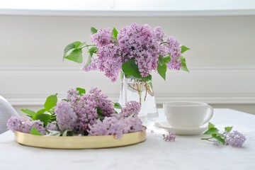 Spring bouquet of lilac flowers in glass jug on table, cup of tea