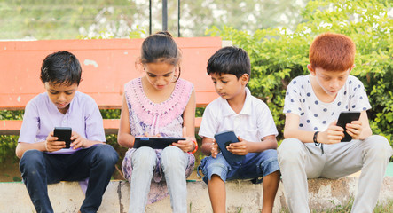 Children busy in using mobile phone at park - Concept of Kids on mobile devices and technology addiction - Young teens using technology, Internet on Smartphone.