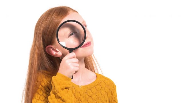 Concept of children's curiosity and education. Adorable little girl with long red hair looking through a magnifying glass, zooming her eye