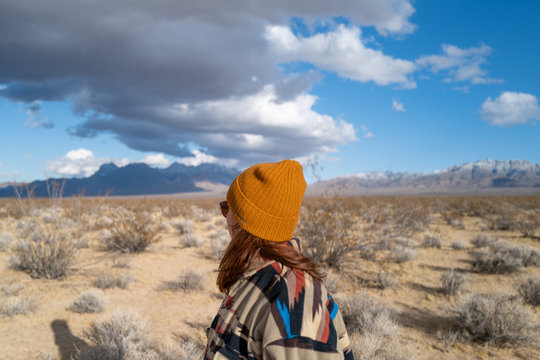 A young woman in a Native American patterned vintage jacket and mustard hat explores sand dunes in California
