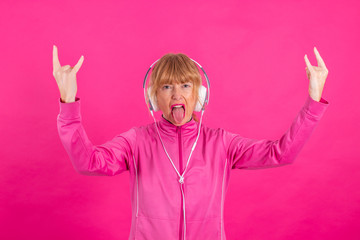 senior woman with headphones and rebel gesture isolated on color background