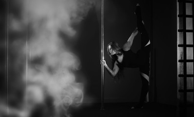 The dancer on the pylon in the studio. Girl doing exercises on a sports equipment.