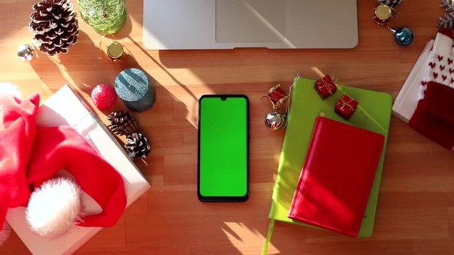 Top view of modern table with chromakey smartphone and. Christmas decoration interior. Happy New Year. Winter holidays celebration. Family internet greeting gift. Green screen mockup. Sunlight. Sunny.