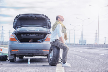 Replacing the wheel of a car on the road. A man doing tire work on the sidelines.