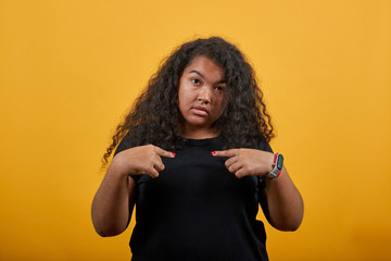 Afro-american young woman with overweight pointing fingers at herself over isolated orange background wearing fashion black shirt. People lifestyle concept.