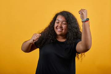 Happy afro-american young woman with overweight keeping fists up, dancing, doing winner gesture...