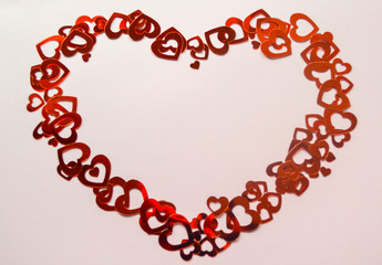 Many bright red shiny hearts of different sizes and shapes make up a huge red heart with an empty space in the middle for the text. Pale pink background. Concept of love, Valentine's day, romance