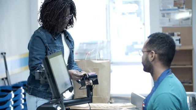 Smiling woman paying with credit card and packing food. Male cashier adjusting card reader for customer and printing receipt. Shopping concept