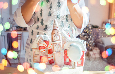 Cake decoration female hands in a frame in a bright kitchen sprinkles gingerbread houses powdered sugar snow Christmas treats for the holiday lights of garlands