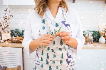 Female hands in the frame hold a sprig of rosemary in a bright kitchen Christmas treat for the holiday lights of garlands