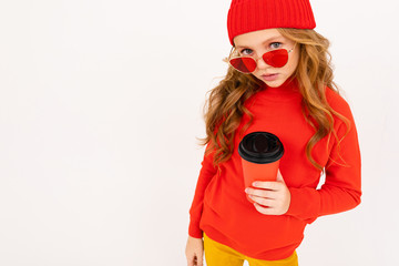 Happy teenager girl with red hair, red glasses smiles and drinks coffee isolated on white background